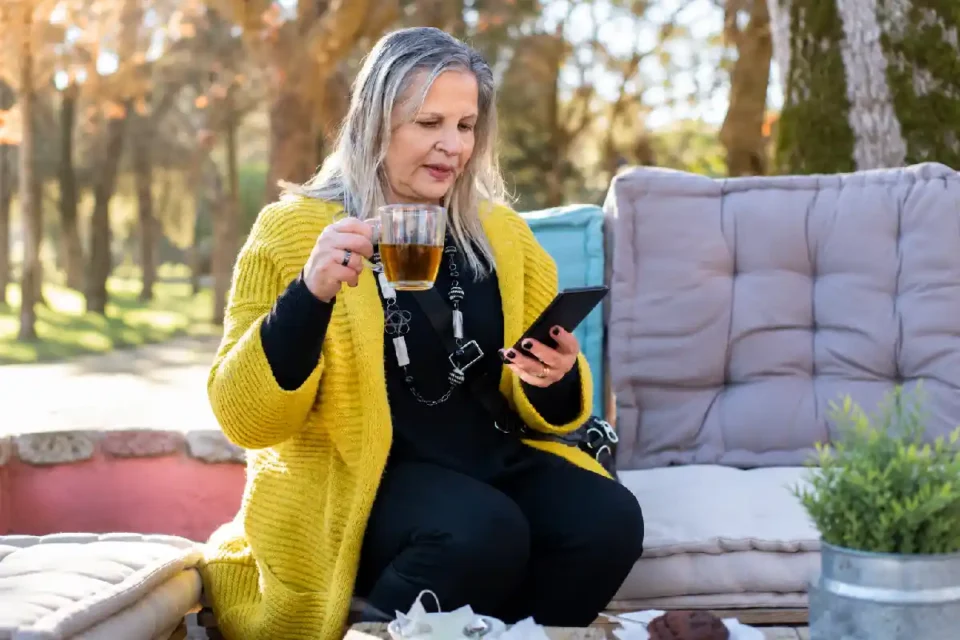 Woman checking her phone while holding a tea cup outdoors